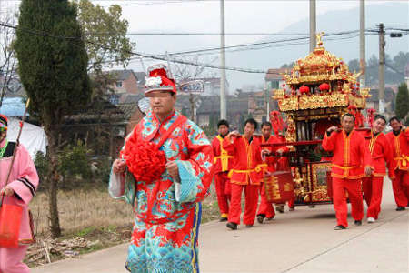 穿着古代吉服的新郎迈着大步走在前面,身后,一顶金花轿在阳光下闪闪