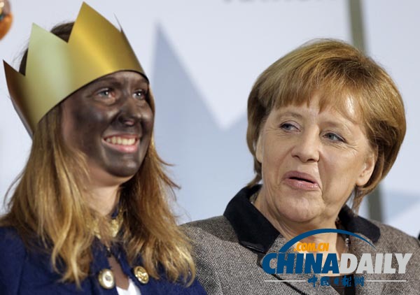 当地时间2013年1月4日，德国柏林，默克尔在总理府招待德国全国圣诞颂歌的吟唱者，看着身旁一名涂成黑脸的女子，想笑又不敢笑。（图片来源：东方IC）