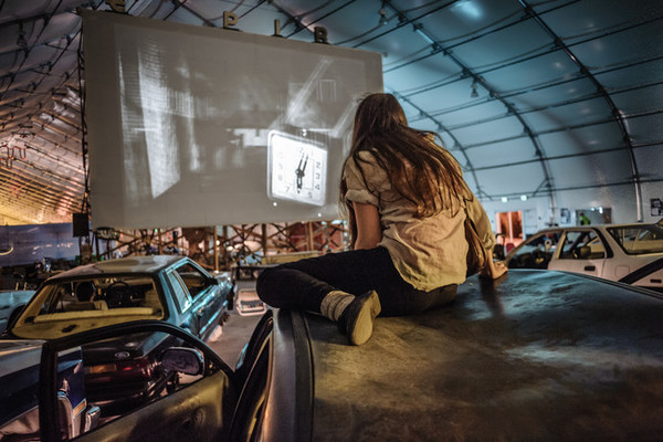 一位女子坐在废弃的汽车影院中观看黑白电影(网页截图)
