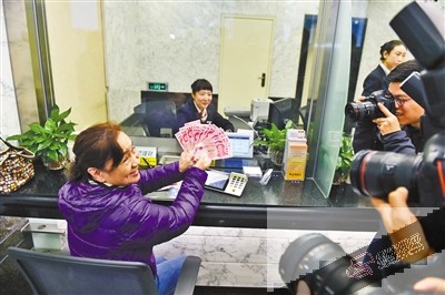 北京的刘女士向记者们展示她刚取的新版百元钞票。