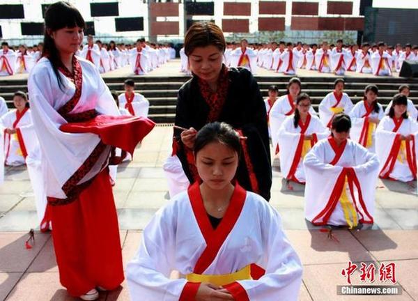 2015年4月21日，湖南省洪江市千名14-24周岁的年轻女子，身穿传统服装，队列整齐，依照古时习俗庄严宣誓，体验成人大典。图为德高望重的长辈为部分女子束起发髻。（图片来源：中新网）