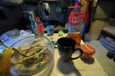图为房子的桌子上，放着大瓶冰红茶，小瓶冰红茶，六神花露水，杯子，矿泉水，养乌龟的鱼缸等。