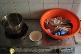 图为煤气灶上放着红色脸盆，里面毛巾、洗面奶、木梳等洗漱用品，旁边的灶台上，放着买来的鸡蛋，另一边的煤气灶上放着锅子。
