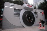 2月6日，重庆市民正经过“照相机”公厕。创意“照相机”厕所亮相重庆石桥铺数码城，以“照相机”外形来修建的公共卫生间，成为一道创意城市风景线。图为市民正经过“照相机”公厕。