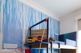 男孩子的卧室就该是灿烂、沉静一定的色调。可以说蓝色是最符合条件的颜色了。背景墙上由深到浅的蓝色天空中夹杂着点点雪花，加上下方穿着红色衣服的卡通人物，和房间中红色的收纳都成了很好的点缀。（实习编辑：温存）