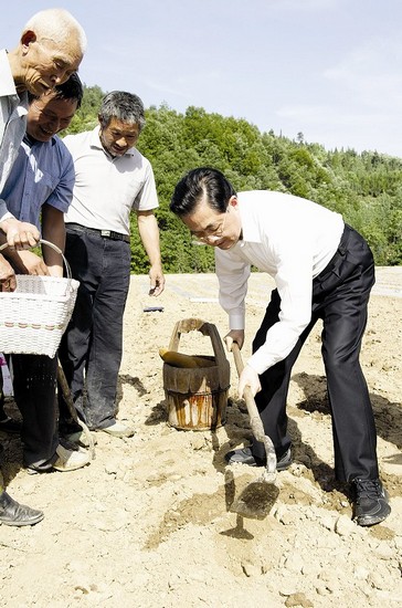 图为：胡锦涛拿着锄头和村民一起补种玉米 新华社资料图片