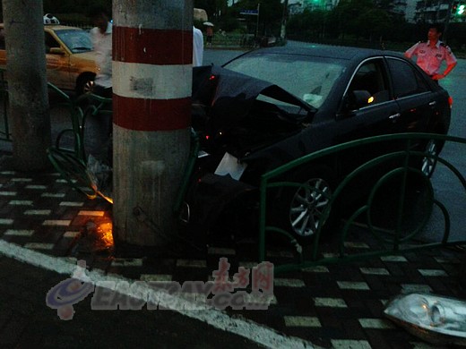图为事发现场轿车撞上路边人行道上的电线杆,车头损毁