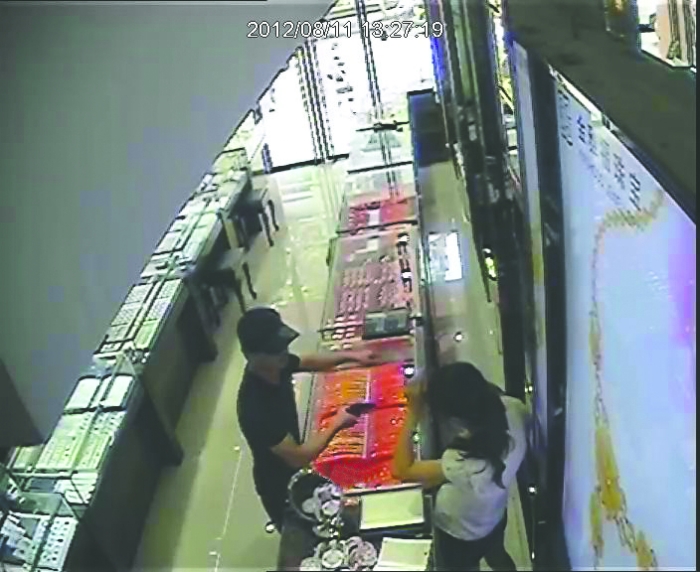 监控记录下劫匪抢劫过程 监控1 下午1时26分56秒 两名男子走进店内。戴着鸭舌帽的男子走在前面,戴头套的男子走在后面。 27分04秒 戴鸭舌帽的男子从裤袋内掏出手枪,后面跟着的男子拿着一把尖刀,径直走向收银台。 27分09秒 戴鸭舌帽的男子用手枪指向店员,左手先指向金饰柜台,接着又指向装金手镯的柜台。 27分21秒 店员站在原地未动,戴鸭舌帽的男子走进柜台内,将店员推到装金手镯的柜台边。 27分35秒 持枪男子又走出柜台,与持刀男子一起走到装金手镯的柜台。 27分47秒 拿刀男子从提包中拿出一个榔头交